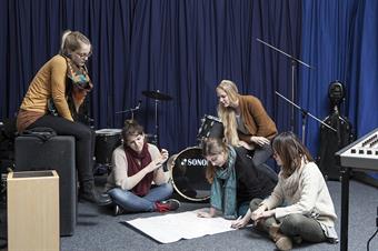 The picture shows a group of female students and a lot of instruments in music studio.